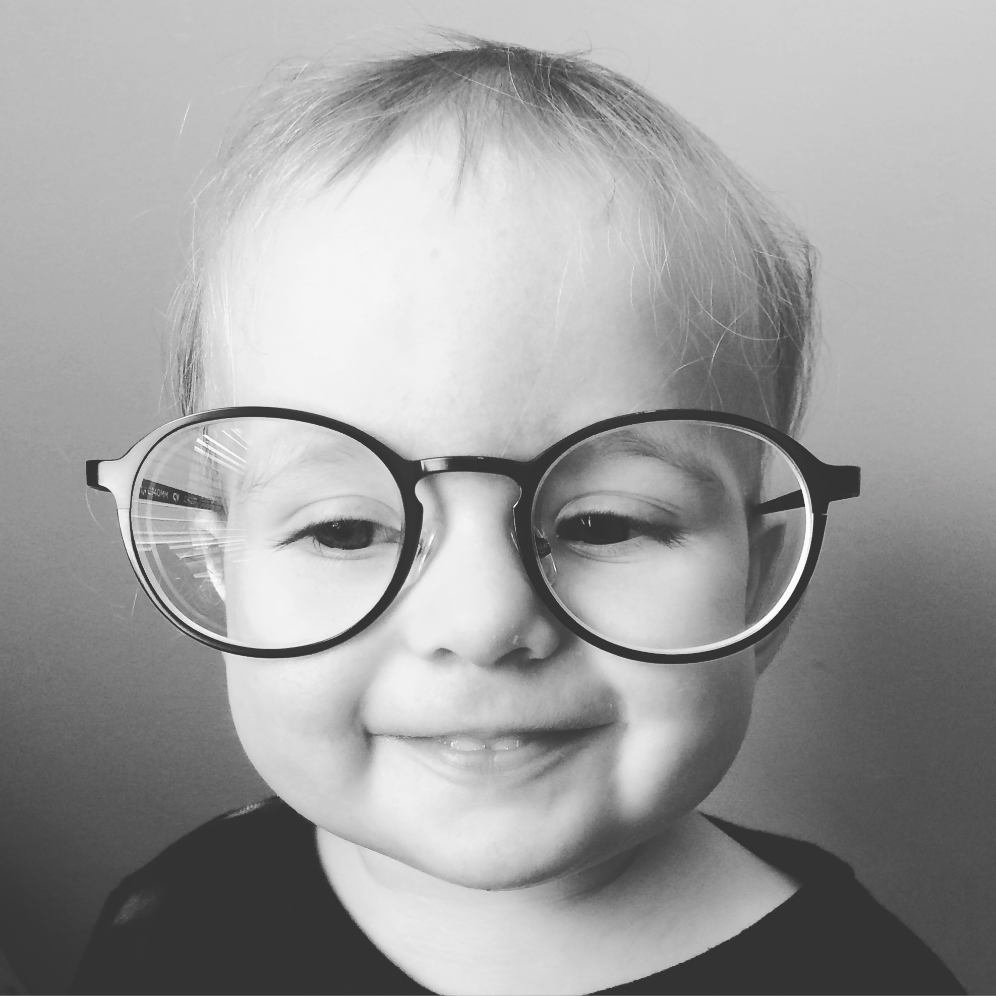 Smiling baby wearing oversized round glasses.