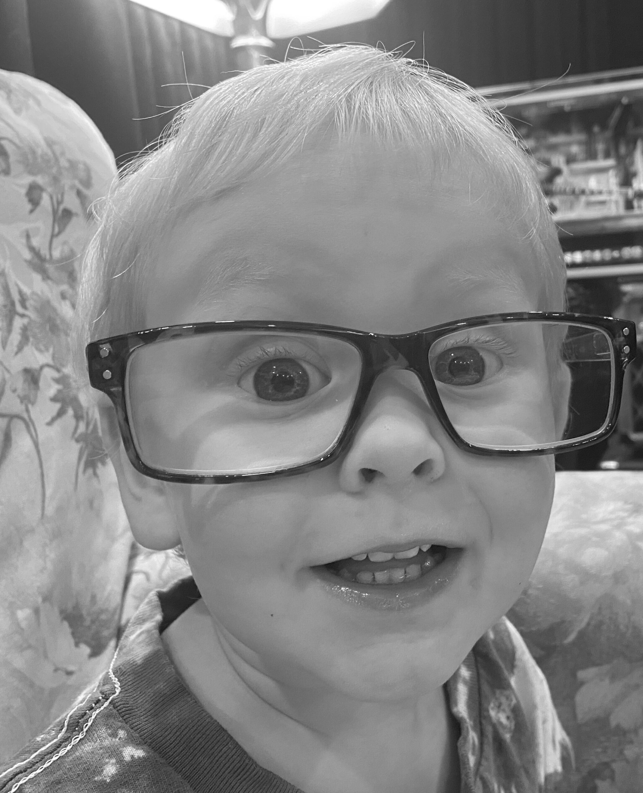 Child wearing oversized glasses, smiling widely.