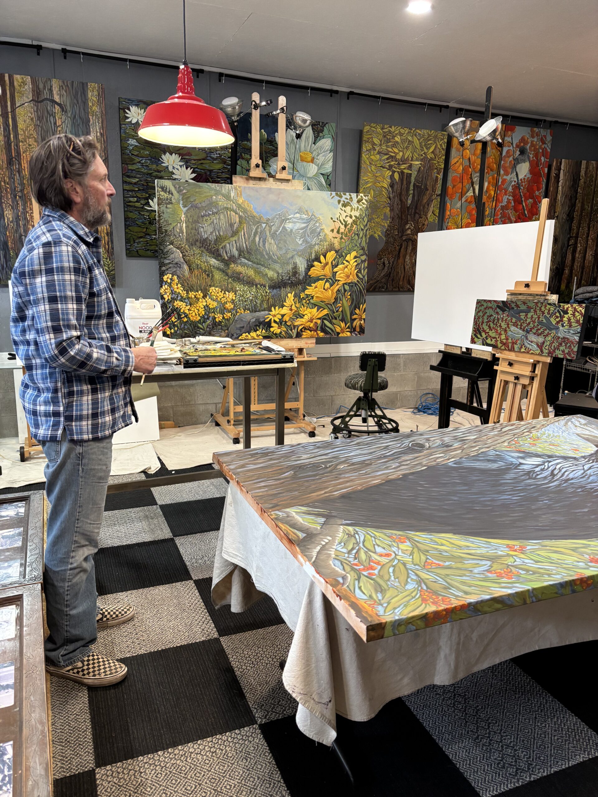 Artist in studio with large landscape paintings.